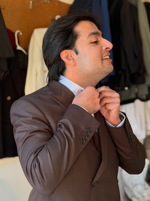 Client adjusting the collar of a brown custom suit jacket during a fitting